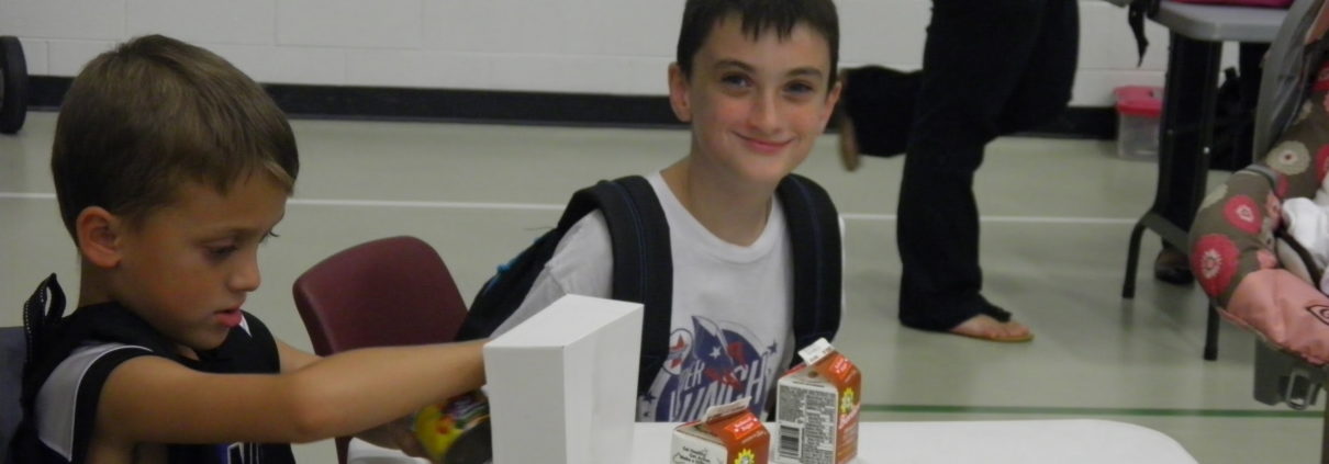Boy smiling at table while grabbing carton